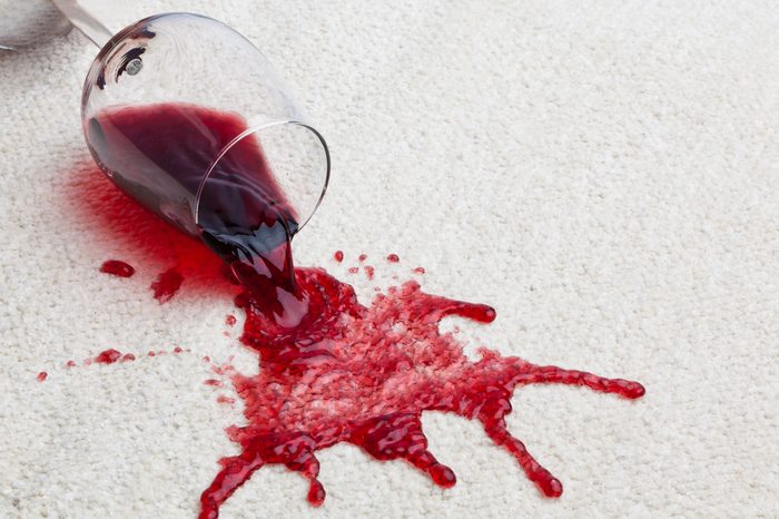 A toppled glass of red wine with a dirty carpet.