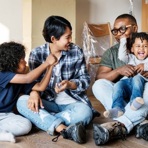 Family sits and laughs together in a room surrounded by cardboard boxes, suggesting a recent move or unpacking process.
