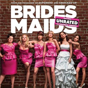 Women pose confidently in pink dresses against a brick wall, promoting the 
