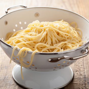 Spaghetti rests in a metal colander on a wooden surface.