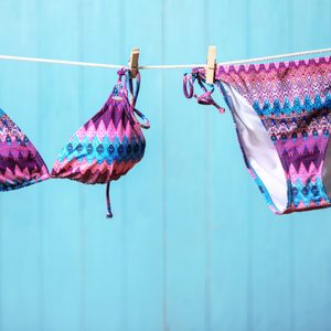 Colorful bikini with geometric patterns hangs on a clothesline against a light blue wooden background.