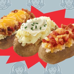 Three baked potatoes, topped with chili, cheese, sour cream, bacon, set against a red burst on a logo-patterned background.