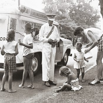 Ice cream truck vendor serves children and adults on a tree-lined street; kids eagerly gather around.