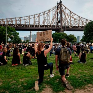 Person kneels, holding sign saying 