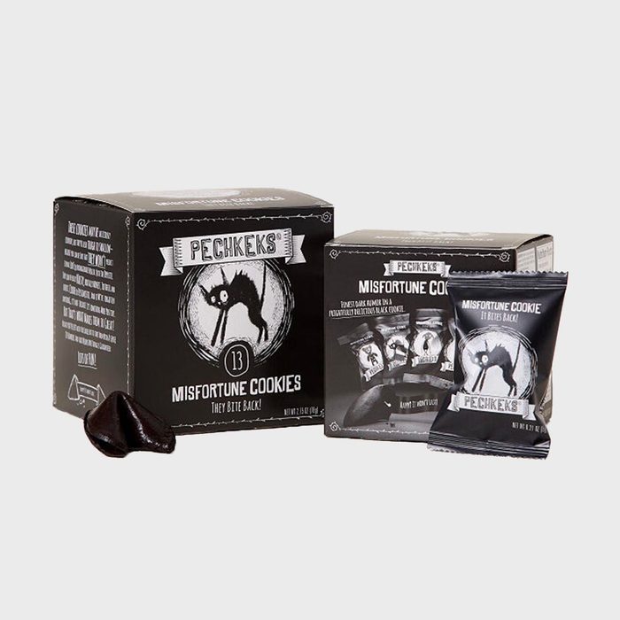 Black misfortune cookies sit in themed packaging featuring a spooky cat, surrounded by individual wrappers, on a plain, light background.