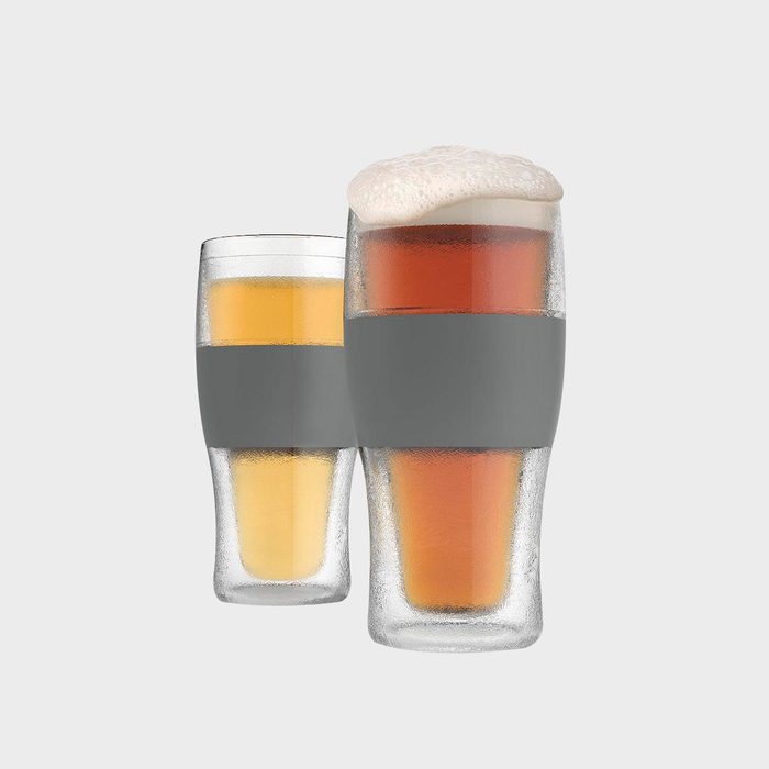 Two frosted glasses hold beer, one with foam, against a plain background. Each has a gray silicone grip around the middle.
