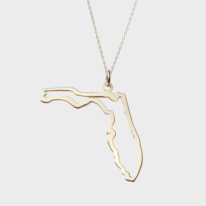 A gold pendant, shaped like Florida, hangs from a delicate chain, set against a plain white background.