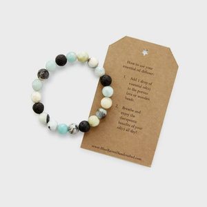 Bracelet lies beside a tag with instructions; add essential oil to beads, breathe in therapeutic benefits. Brown tag provides detailed steps for usage.
