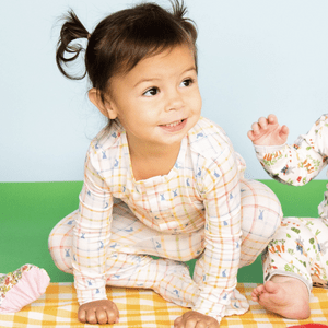 Child smiling, wearing colorful pajamas, sitting on a checkered blanket.