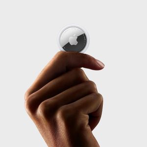 Hand holding a circular, metallic object with an Apple logo, against a plain background.