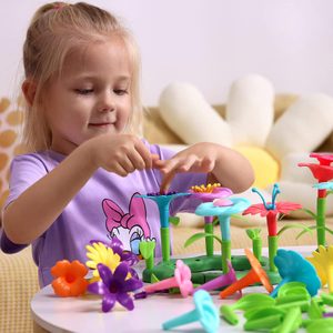Child assembles colorful plastic flowers on a table, sitting in a cozy room with a floral-themed backdrop.