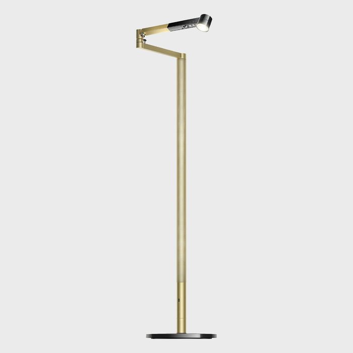 Gold floor lamp stands upright, projecting light from an adjustable arm, set against a plain white background.