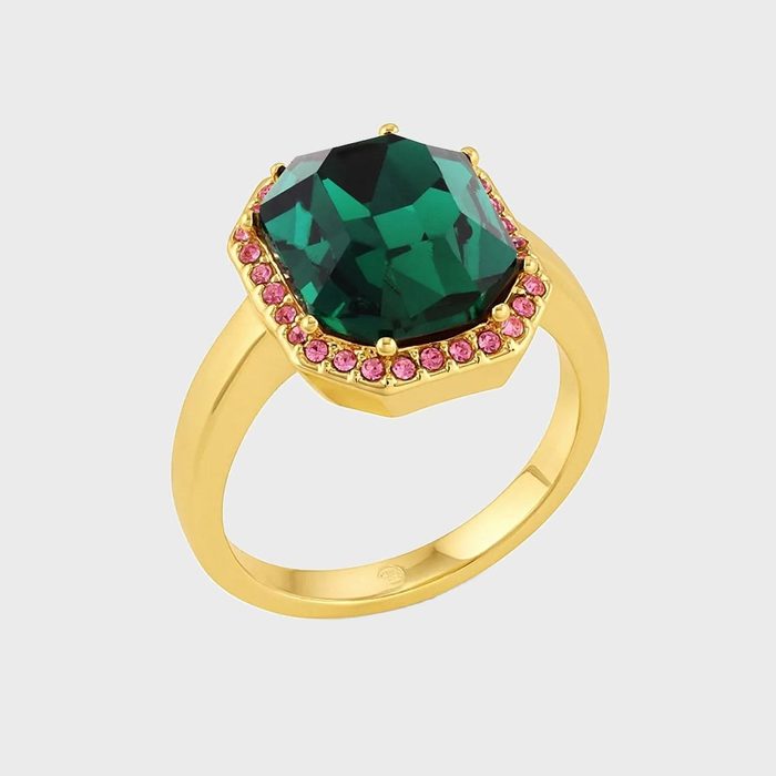 A gold ring features a large emerald-like stone surrounded by small pink gems, set against a plain white background.