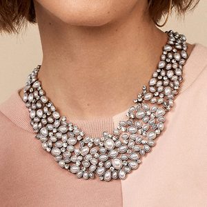Necklace adorned with pearls and crystals, resting on a person wearing a pink top, surrounded by soft lighting.
