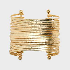 A wide, textured gold bracelet with multiple horizontal bands curves slightly, featuring spherical ends, against a plain white background.