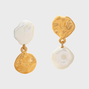 Golden and pearly earrings hang against a plain background, showcasing their unique irregular shapes and contrasting textures.