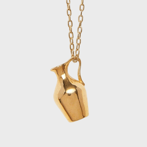 A gold necklace pendant shaped like a small jug hangs from a chain against a plain white background.