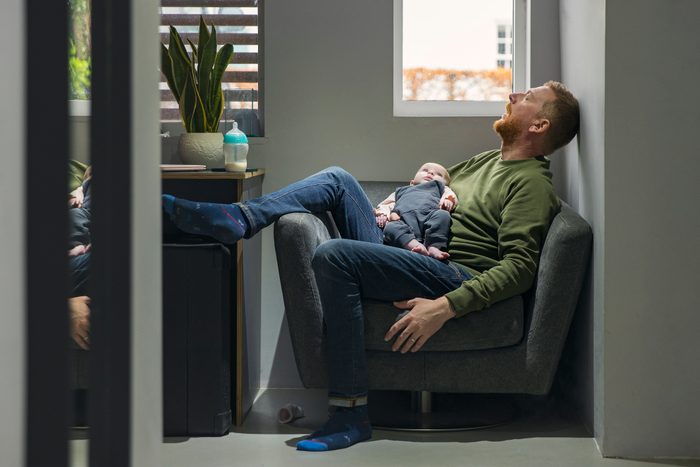 Mature man sleeps on the armchair whilst he holds his baby daughter