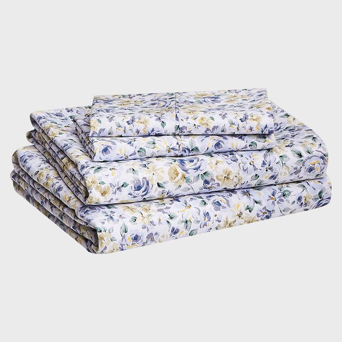 Floral bed sheets stacked neatly, featuring blue and yellow flowers, set against a plain gray background.
