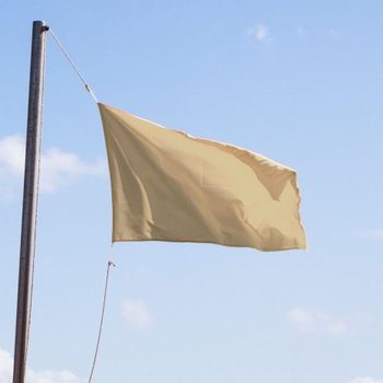 A beige flag waves on a pole against a clear blue sky dotted with small clouds.