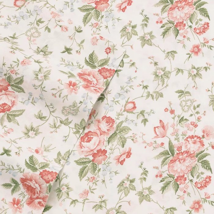 Fabric showcases pink and green floral pattern on an ivory background, creating a vintage, elegant design suitable for home decor or fashion.