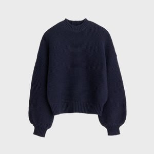 A navy blue, textured knit sweater with long sleeves and ribbed cuffs is displayed against a plain gray background.