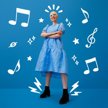 Person smiling confidently, standing with arms crossed, wearing a textured blue dress and black boots, surrounded by white musical notes and stars, against a blue background.