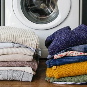Folded clothes sit in piles on a wooden floor, in front of a washing machine.
