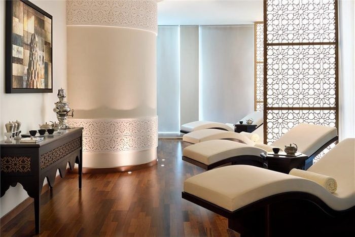 Chaises lounge rest in a serene room with ornate screens and a console table holding tea sets, evoking a peaceful, spa-like ambiance.