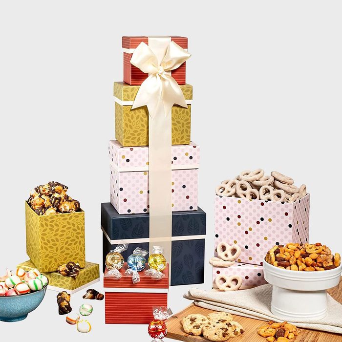 Stacked gift boxes adorned with a bow, revealing various snacks like pretzels, cookies, and chocolates on a wooden surface.