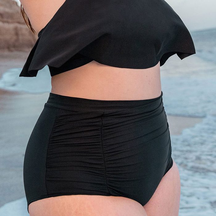 Black swimsuit is worn by a person standing by the ocean on a sandy beach.