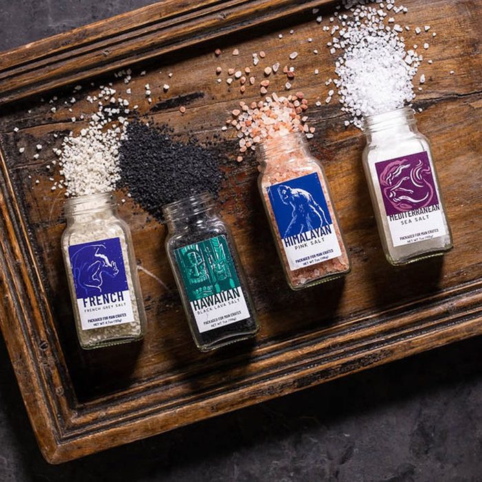 Salt jars spill different colored salts on a wooden tray. Labels read: 