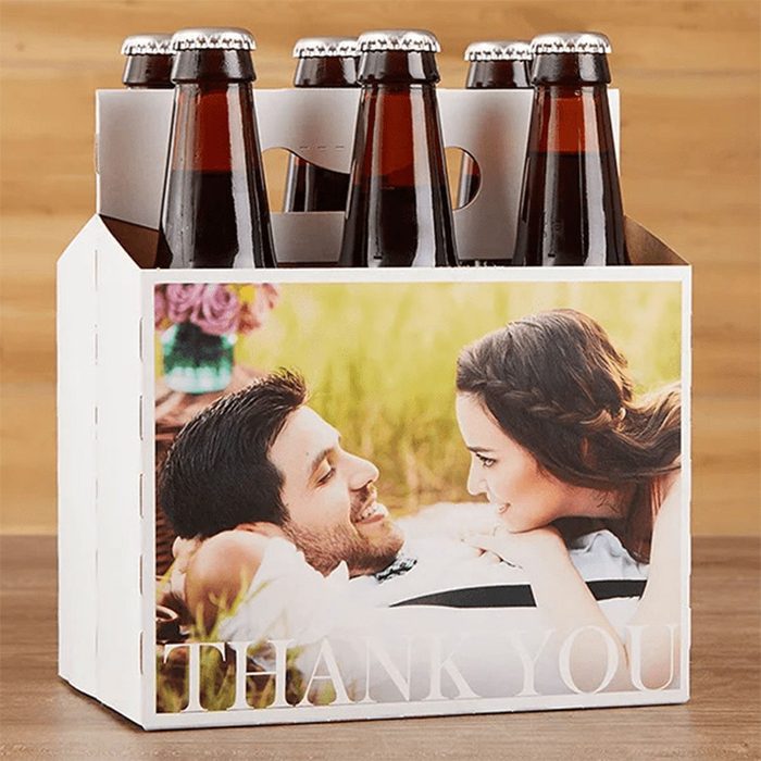 Six-pack of beer bottles resting on a table, features an image of a smiling couple and text 