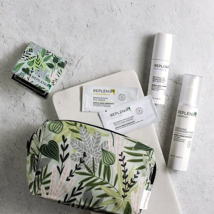 Skincare products arranged on a light surface, including tubes, packets, and a leafy-patterned bag, conveying a clean, botanical theme.