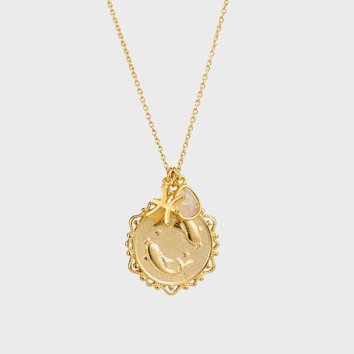 Gold necklace displays a round pendant with fish engravings, accompanied by a small gemstone and starfish charm, set against a plain background.