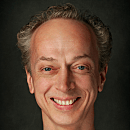 A person with a smile stands against a dark, textured background, exuding a friendly and approachable demeanor.