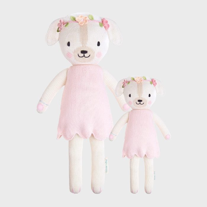 Two plush dogs wear pink dresses and floral headbands, standing side by side, against a plain gray background.