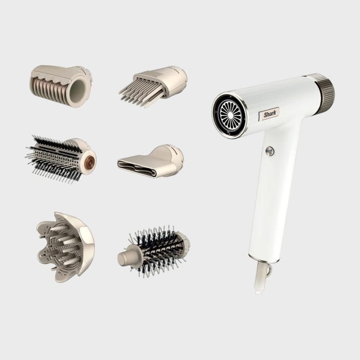 Hair dryer sits surrounded by six interchangeable styling attachments against a plain backdrop.