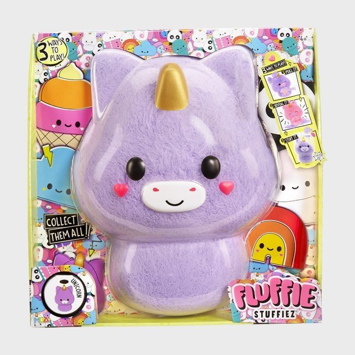 A plush purple unicorn toy is displayed in a colorful package featuring cartoon characters and text like 