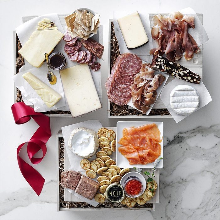 Cheese and meat are arranged on boxes with crackers, smoked salmon, and caviar; a red ribbon adds a decorative touch on a marble surface.