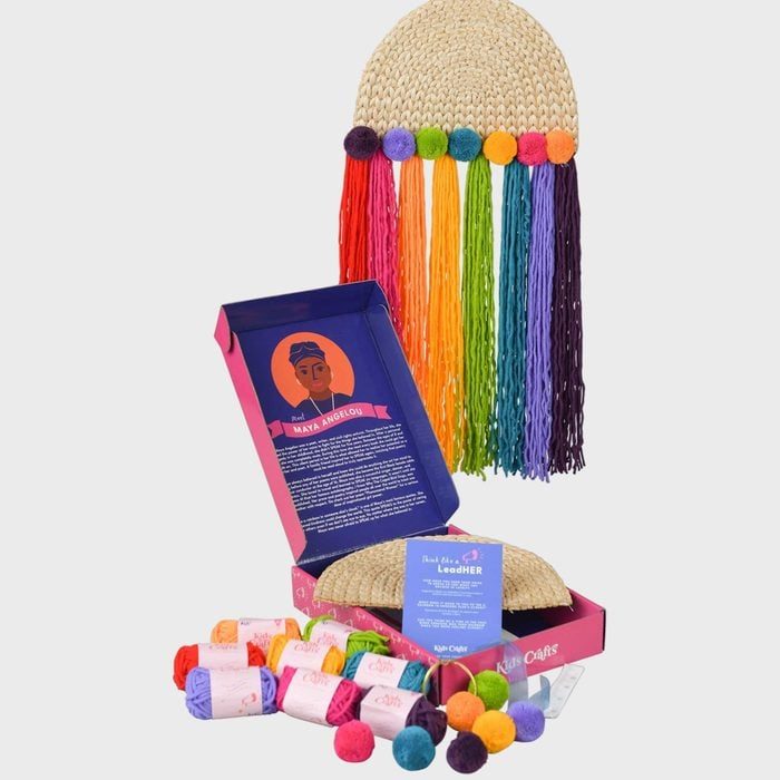 A straw hat features hanging rainbow threads with pom-poms. Below, an open box reveals colorful yarn and text about Maya Angelou on a card.