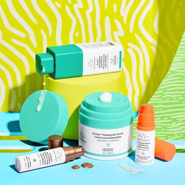 Skincare products displayed on a colorful background. Creams and serums are arranged with visible textures and vibrant packaging against a patterned yellow and green backdrop.