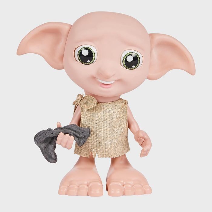 Elf-like doll holds a gray sock, smiling; wearing a simple fabric tunic. Set against a plain white background.