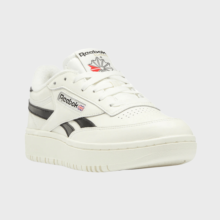 White sneaker displayed, showing Reebok logo with black stripes; positioned against a plain grey background.