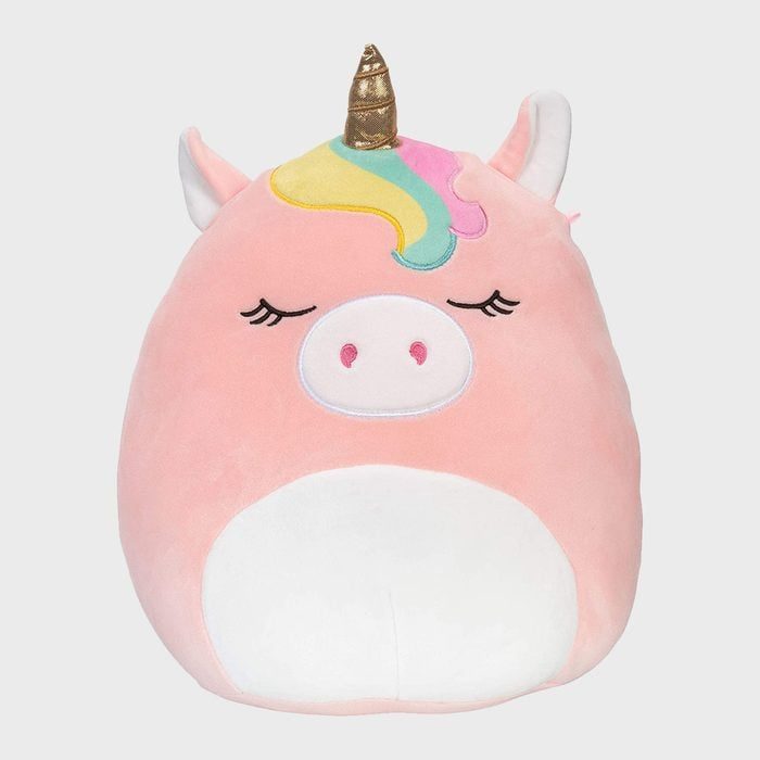 A plush unicorn pillow sits against a plain background, featuring closed eyes, a rainbow mane, and a golden horn.