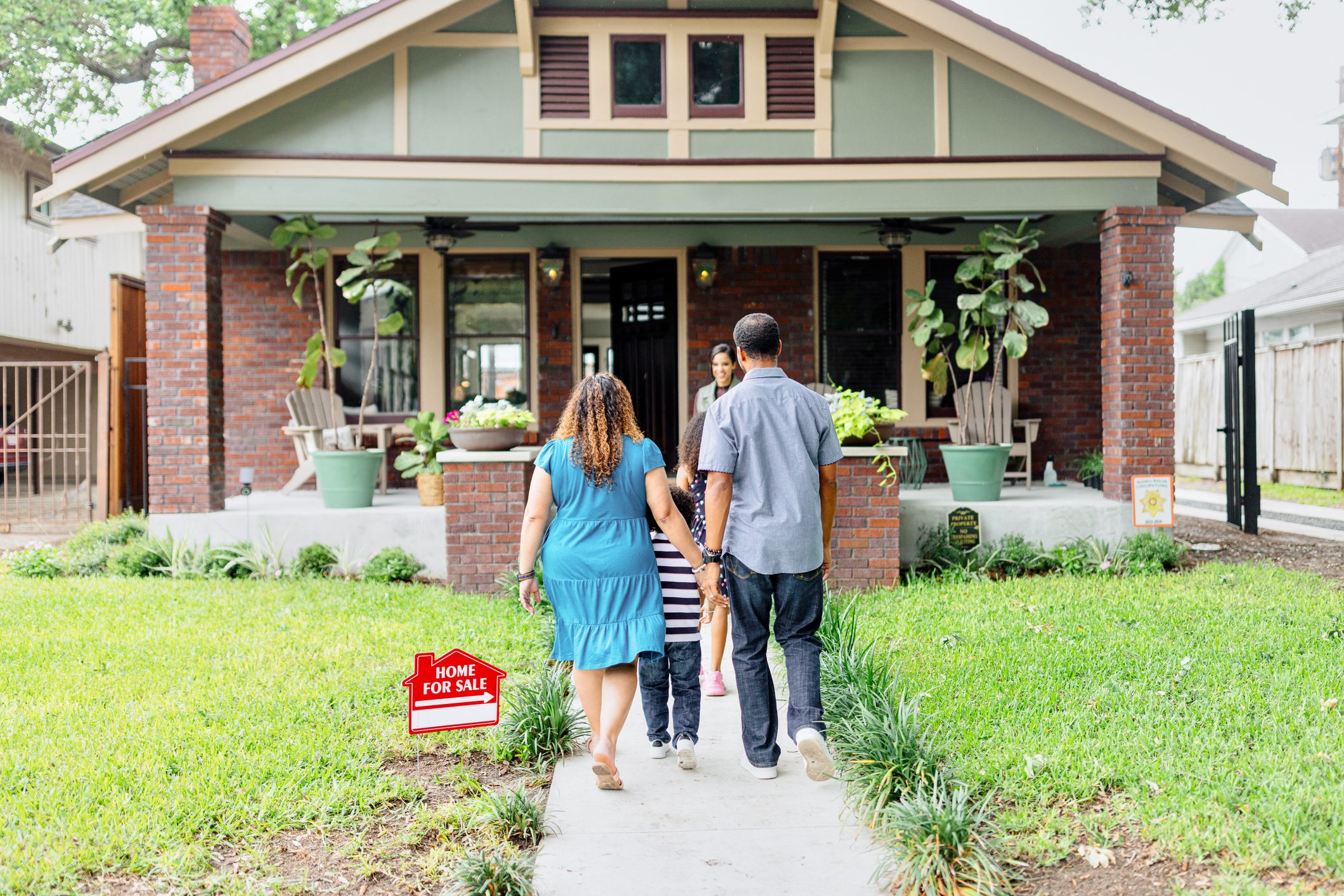 A family of three meeting with a real estate agent in front of a house on sale