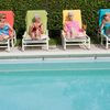 Four women on multicolored towels and pool lounge chairs next to a pool